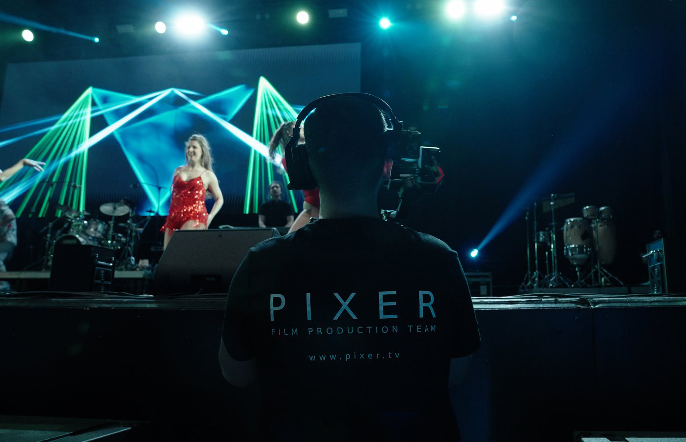 Pixer Film Production Team member filming a live concert with green geometric laser show on stage
