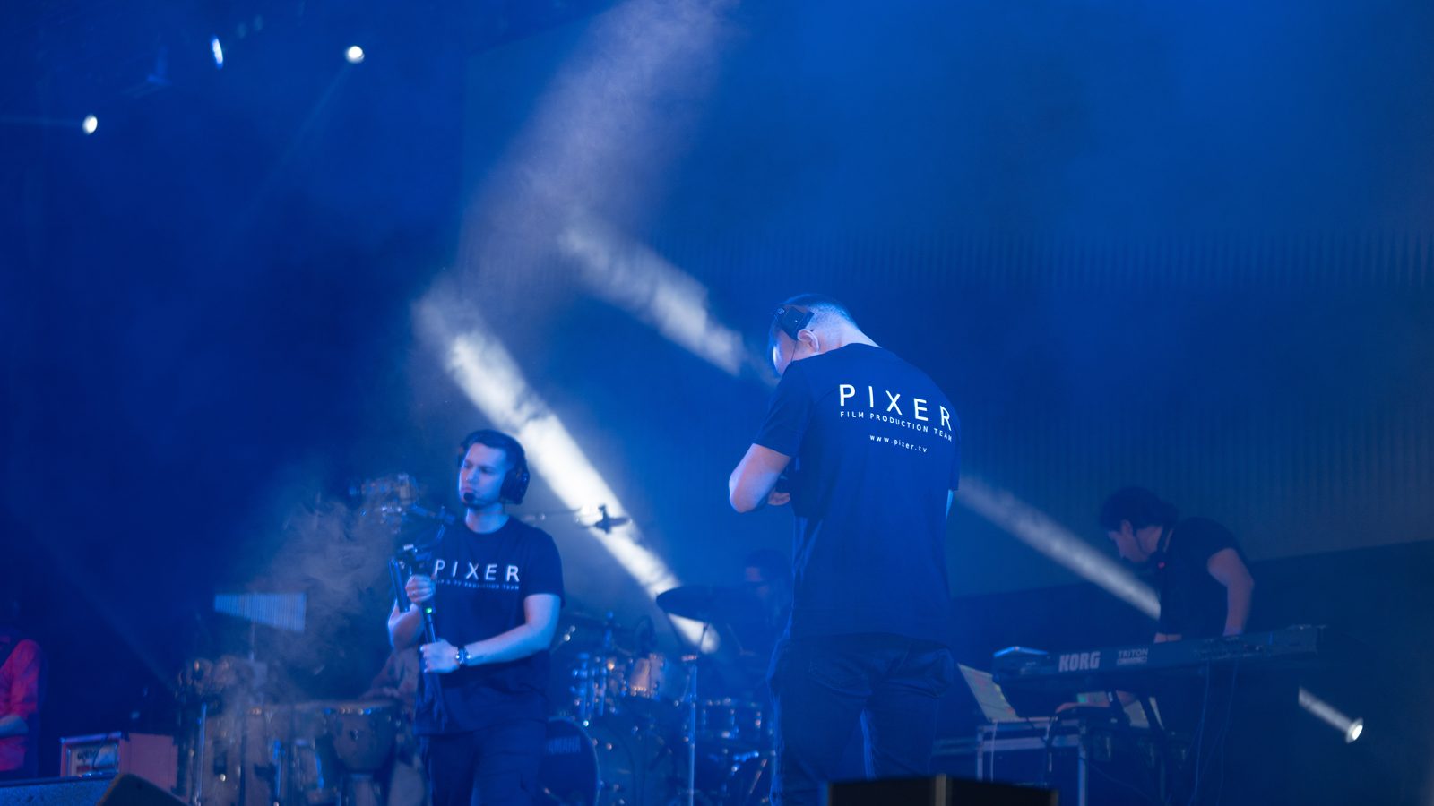 Pixer film production crew on stage during a live concert with dramatic blue stage lighting